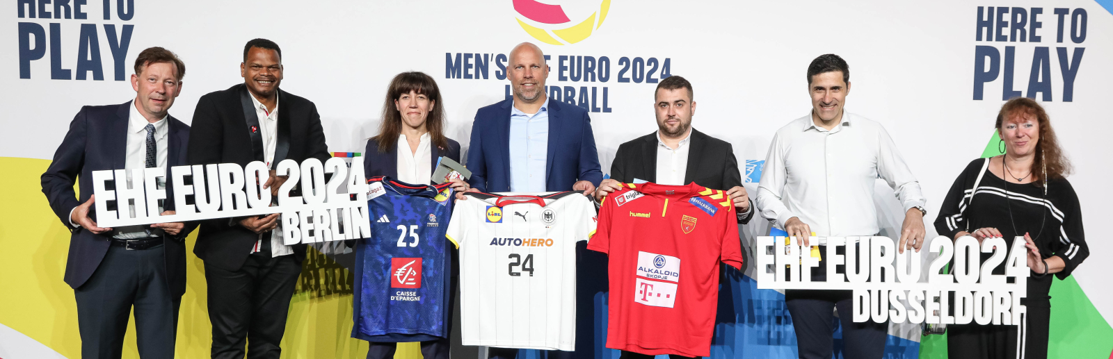 Menschen vor Sponsorenwand der EHF EURO 2024