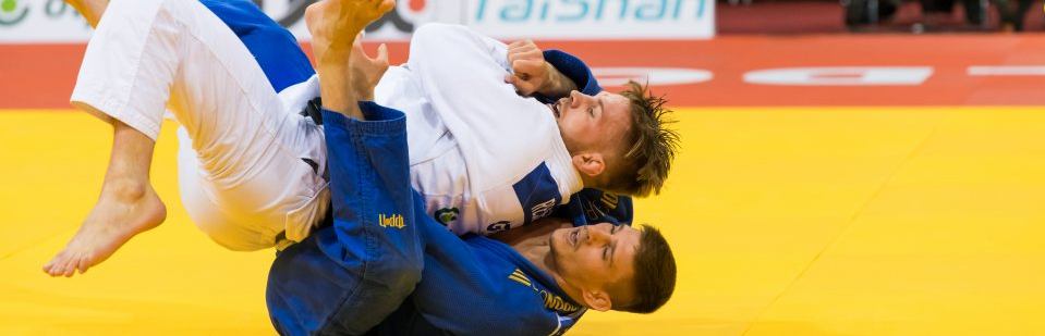 zwei Judoka kämpfen auf einer gelben Matte