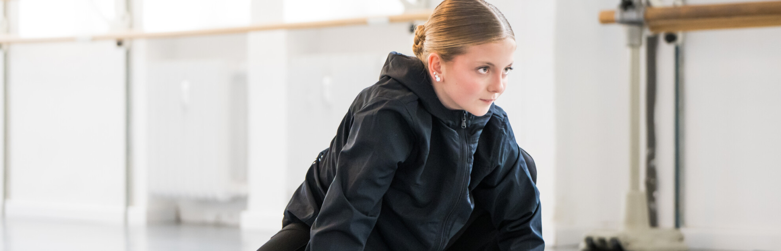 Junge Frau in dunkler Kleidung in Tanzpose mit Händen auf dem Boden in einem Studio