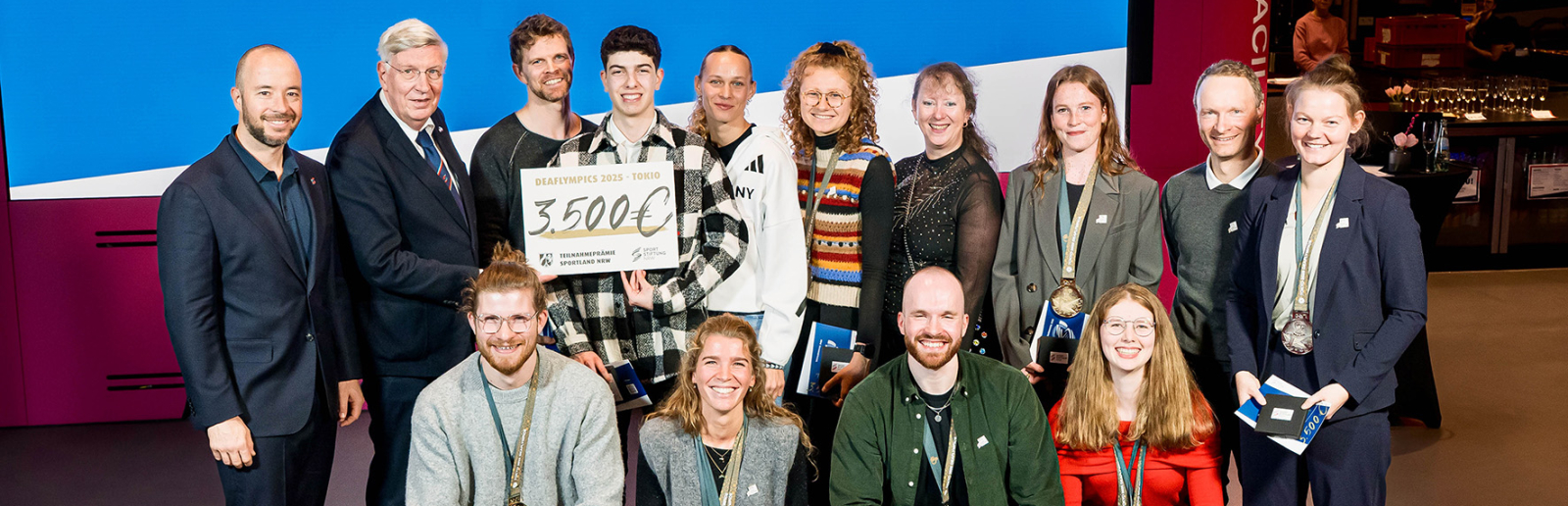 Mehrere Personen in zwei Reihen hintereinander vor einem großen blauen Banner mit 45.500 Euro