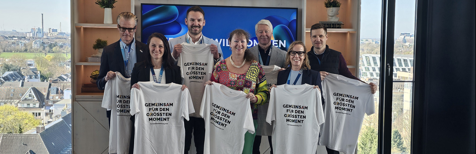Mehrere Personen halten helle T-Shirts hoch, im Hintergrund ein Fenster