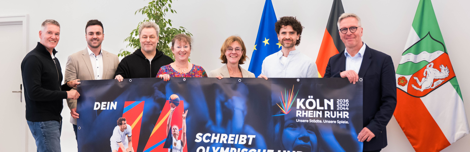 Sieben Personen, darunter Andrea Milz, halten ein Plakat zur Bewerbung KölnRheinRuhr