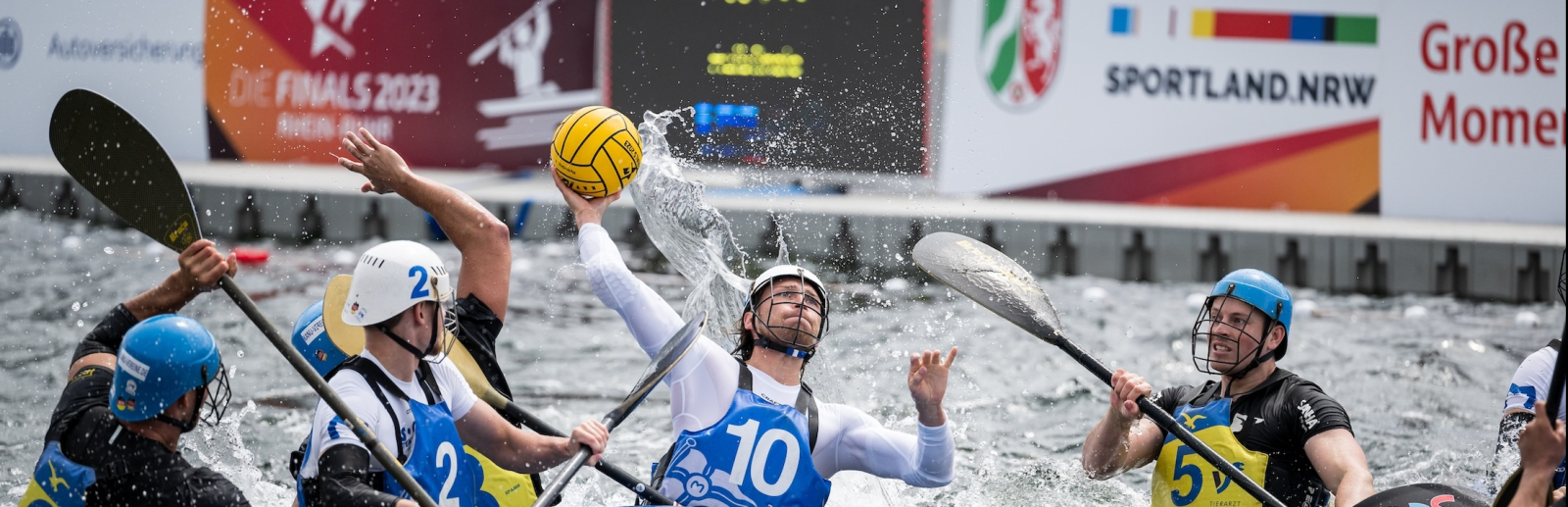 Kanufahrer auf dem Wasser mit einem Banner "Sportland.NRW" im Hintergrund