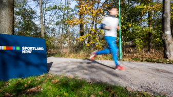 Ein Jogger läuft an einem Sportland.NRW-Schild vorbei