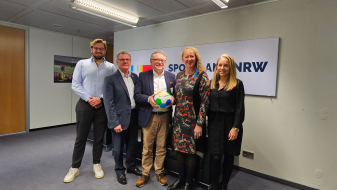 Fünf Personen in einem Flur vor Sportland.NRW Banner 