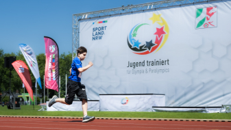 Läufer auf roter Tartanbahn vor einem Banner von Jugend trainiert