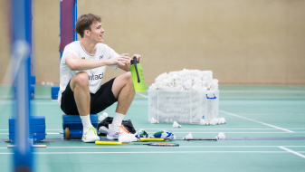 Linus sitzt mit angezogenen Knien in der Badmintonhalle am Netz