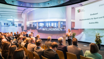 Andrea Milz auf einer Bühne mt Sitzreihen voller Personen