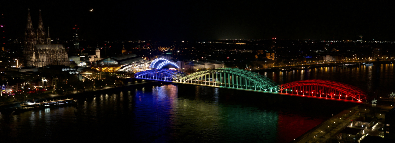 Bunt erleuchtete Brücke vor der Skyline von Köln