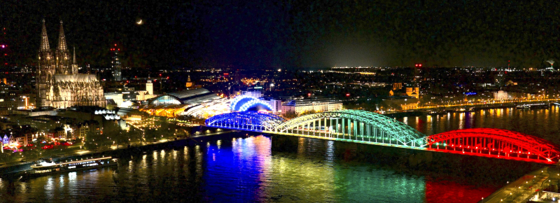 Bunt erleuchtete Brücke vor der Skyline von Köln